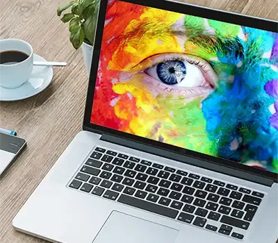 Laptop with an image of a close up of a blue eye on a face painted all the colours of the rainbow